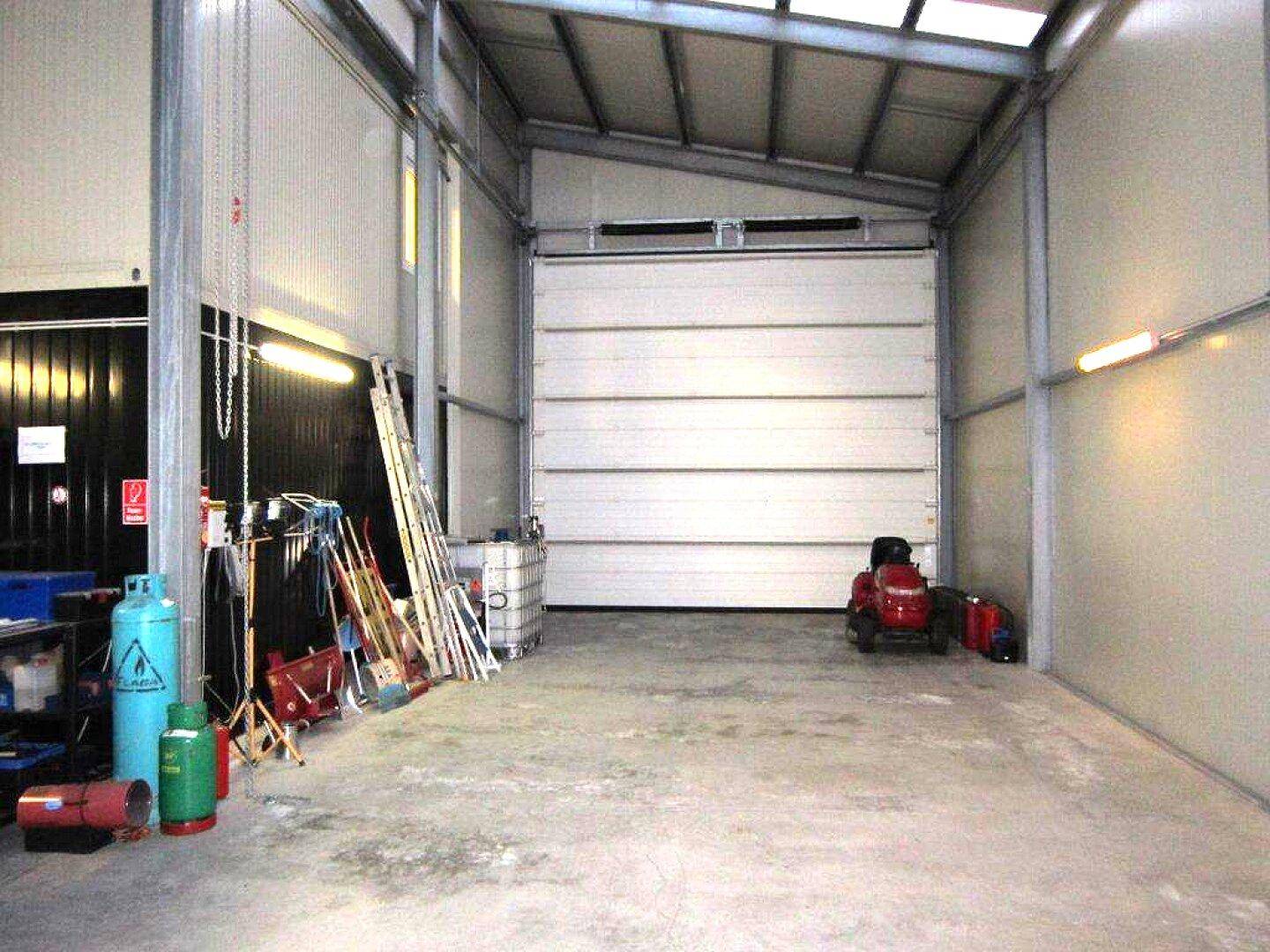 Geräumige Lagerhalle mit Betonboden, einem großen Rolltor und verschiedenen Werkzeugen und Geräten.