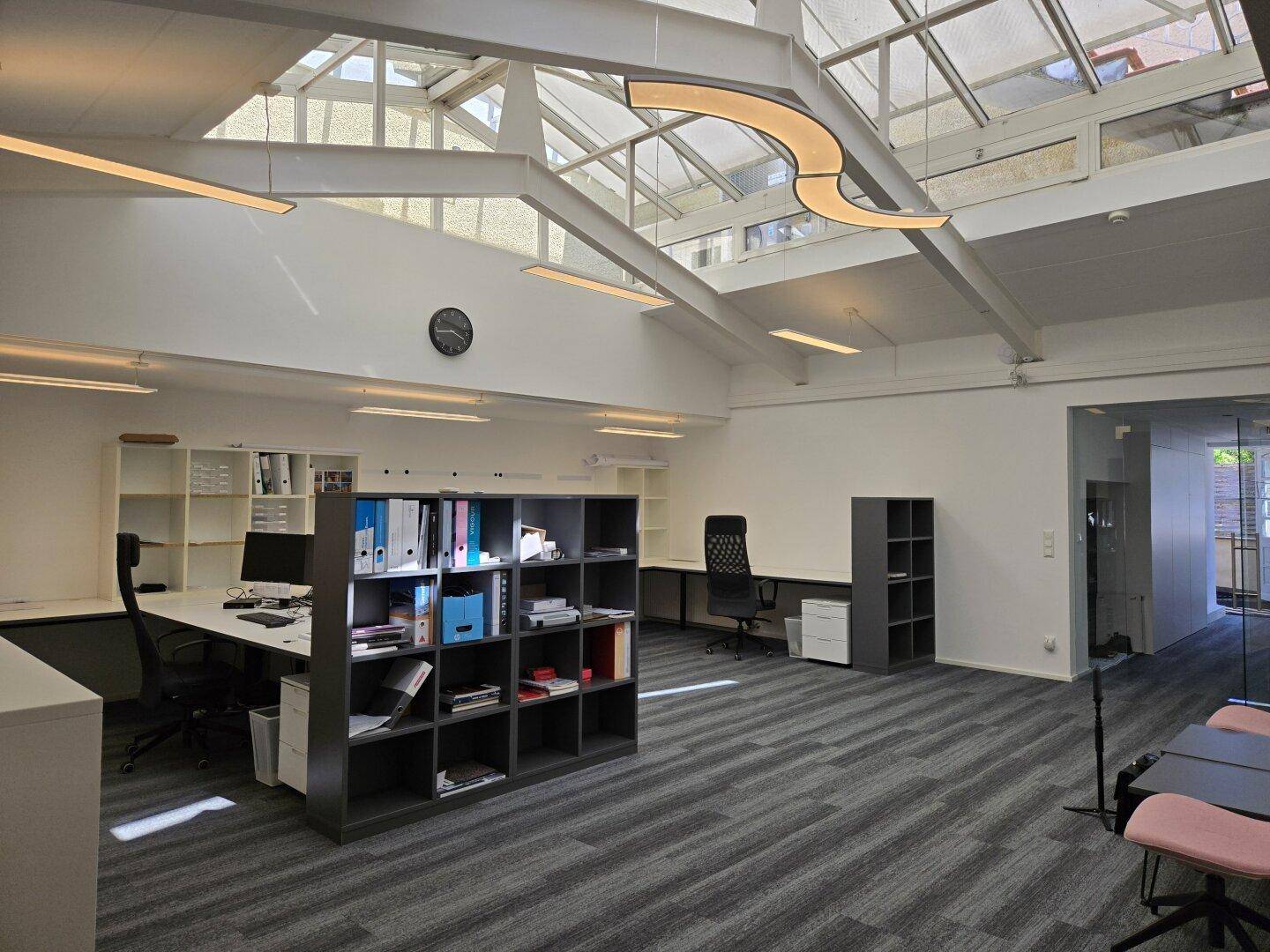 Geräumiges Büro mit mehreren Arbeitsplätzen, Glasdach und moderner Beleuchtung.