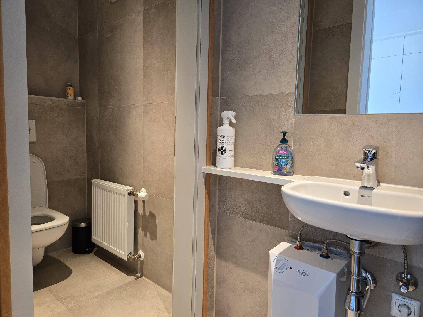 Modernes Badezimmer mit grauen Fliesen, wandhängendem WC und Heizkörper.