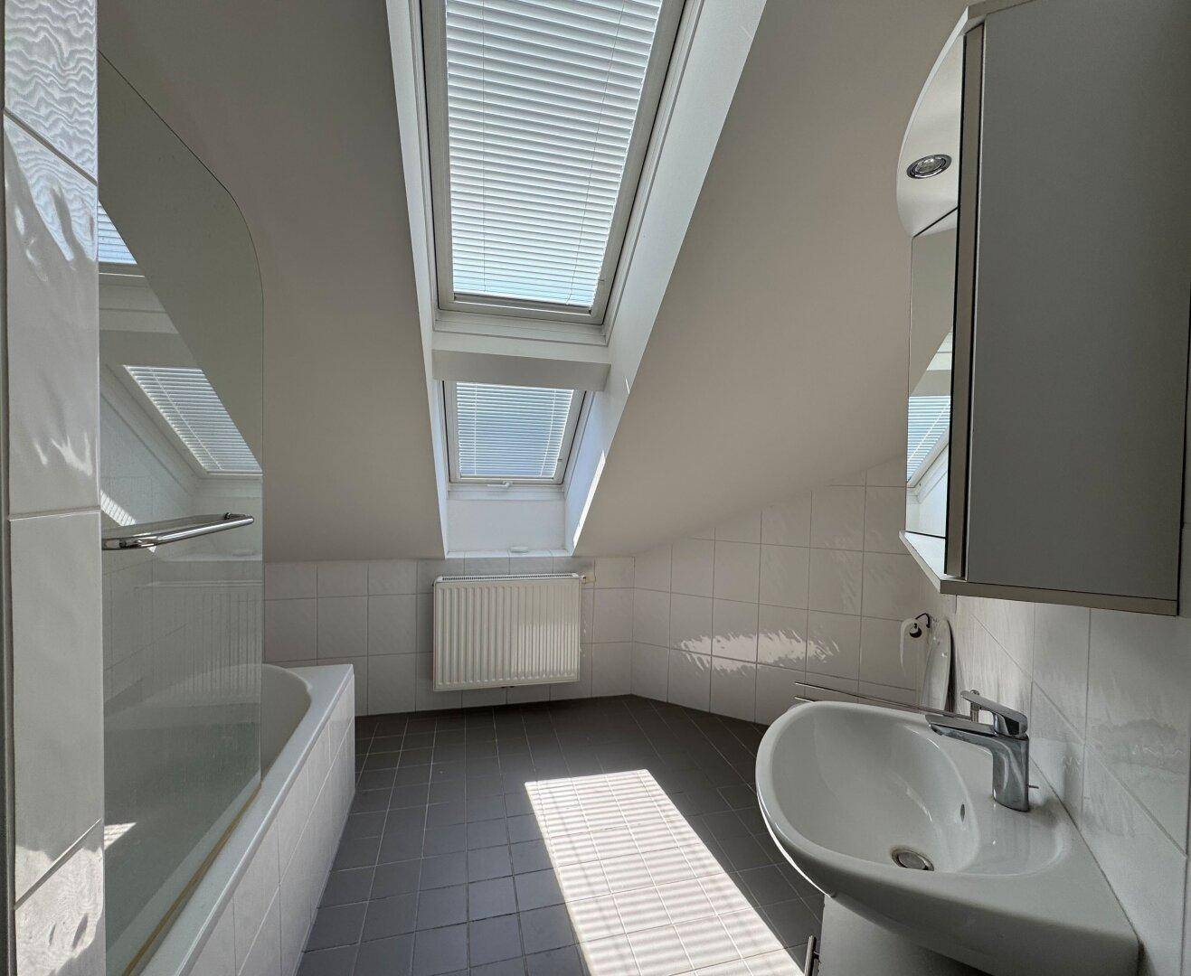 Modernes Badezimmer im Dachgeschoss mit Badewanne, Waschbecken und zwei Dachfenstern.