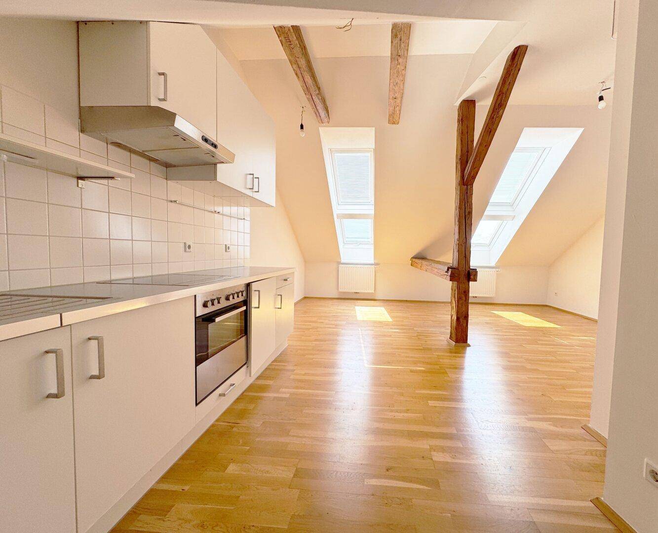 Offener Wohnbereich im Dachgeschoss mit integrierter Küche, Dachfenstern und Holzbalken.
