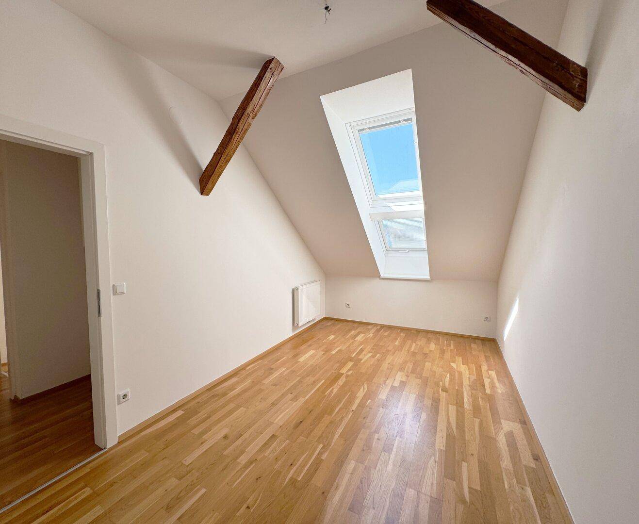 Gemütliches Schlafzimmer im Dachgeschoss mit Parkettboden, Holzbalken und Dachfenster.
