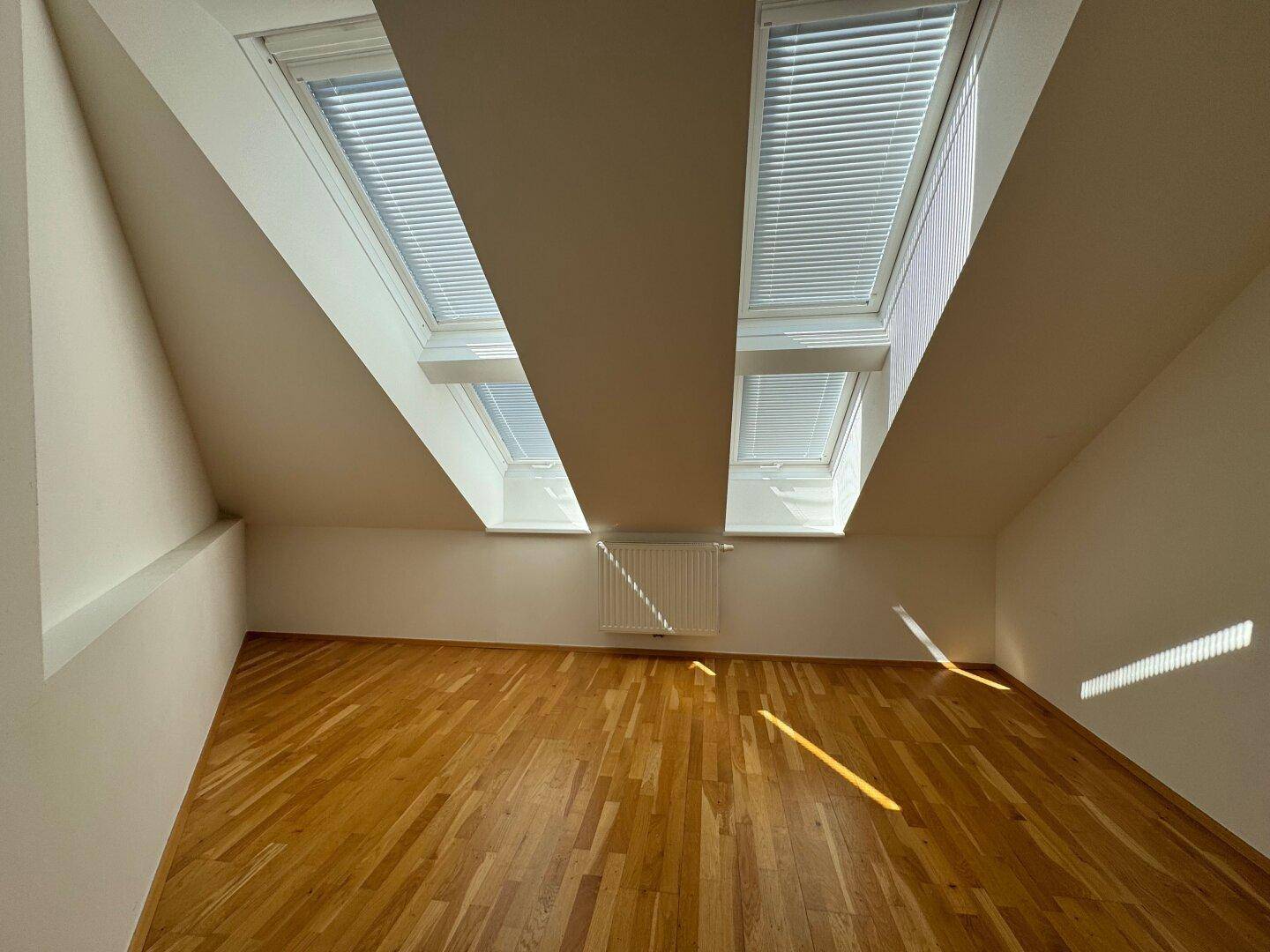 Helles Schlafzimmer im Dachgeschoss mit zwei Dachfenstern und warmem Parkettboden.