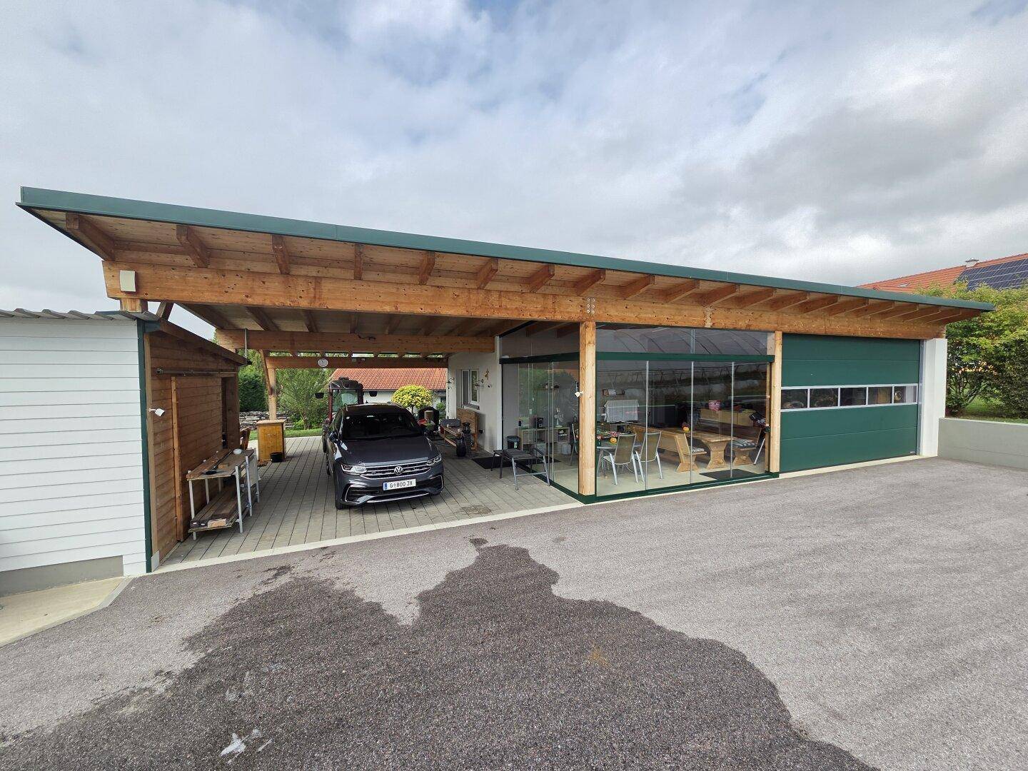 Außenansicht des Hauptgebäudes mit Carport, geparktem Auto und dem verglasten Wintergartenbereich.