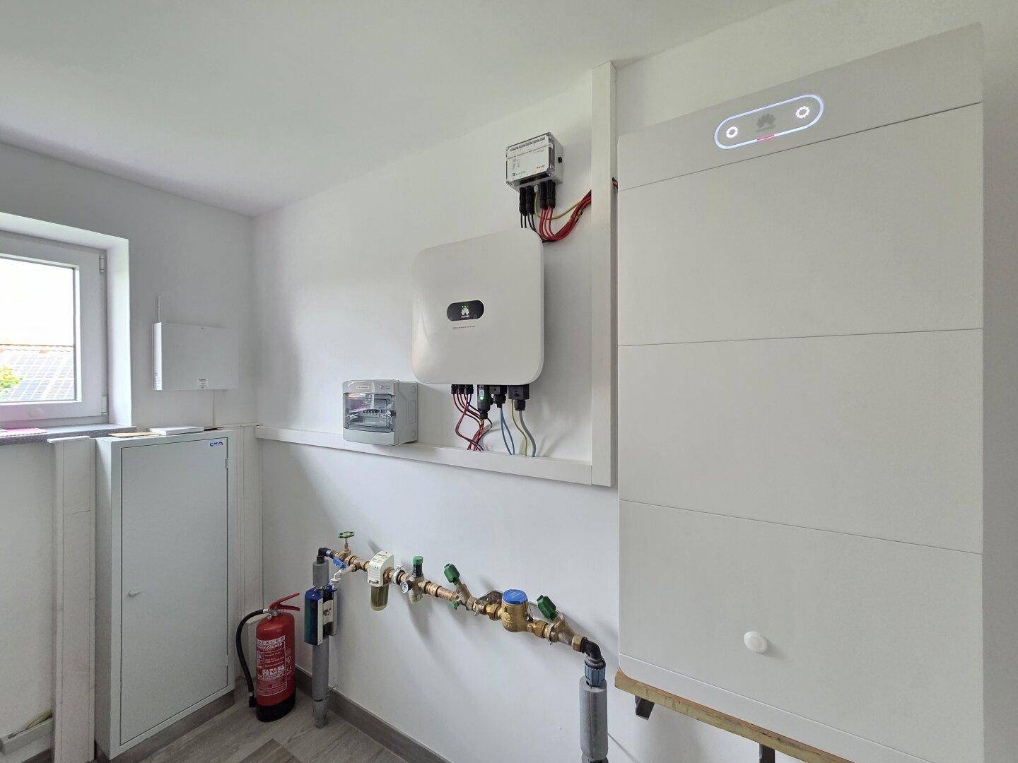 Technikraum mit Fenster, Rohrleitungen und einem modernen Batteriespeichersystem für die Energieversorgung.
