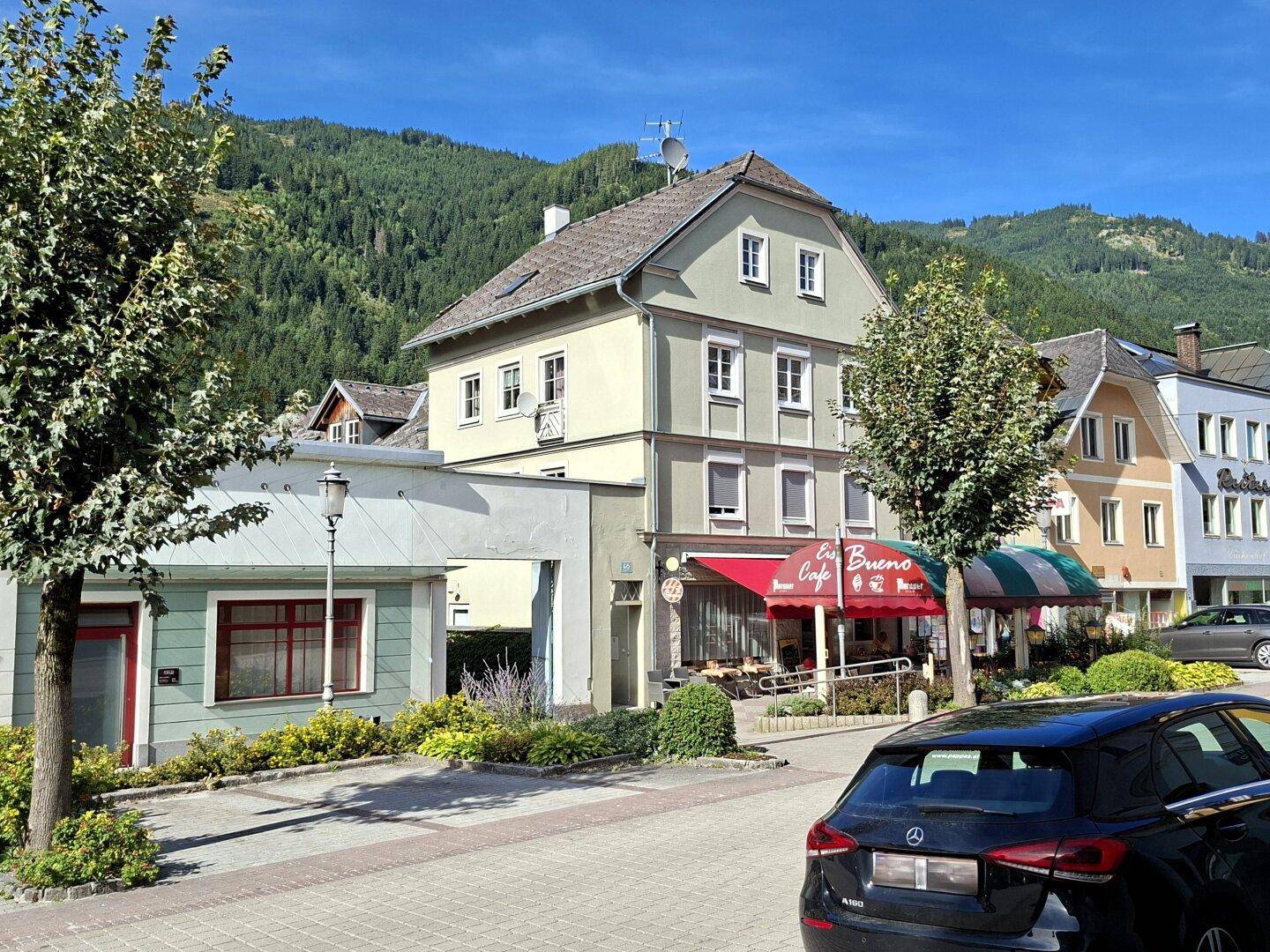 Malerische Straße mit Gebäuden, Geschäften und Bergen im Hintergrund unter blauem Himmel.