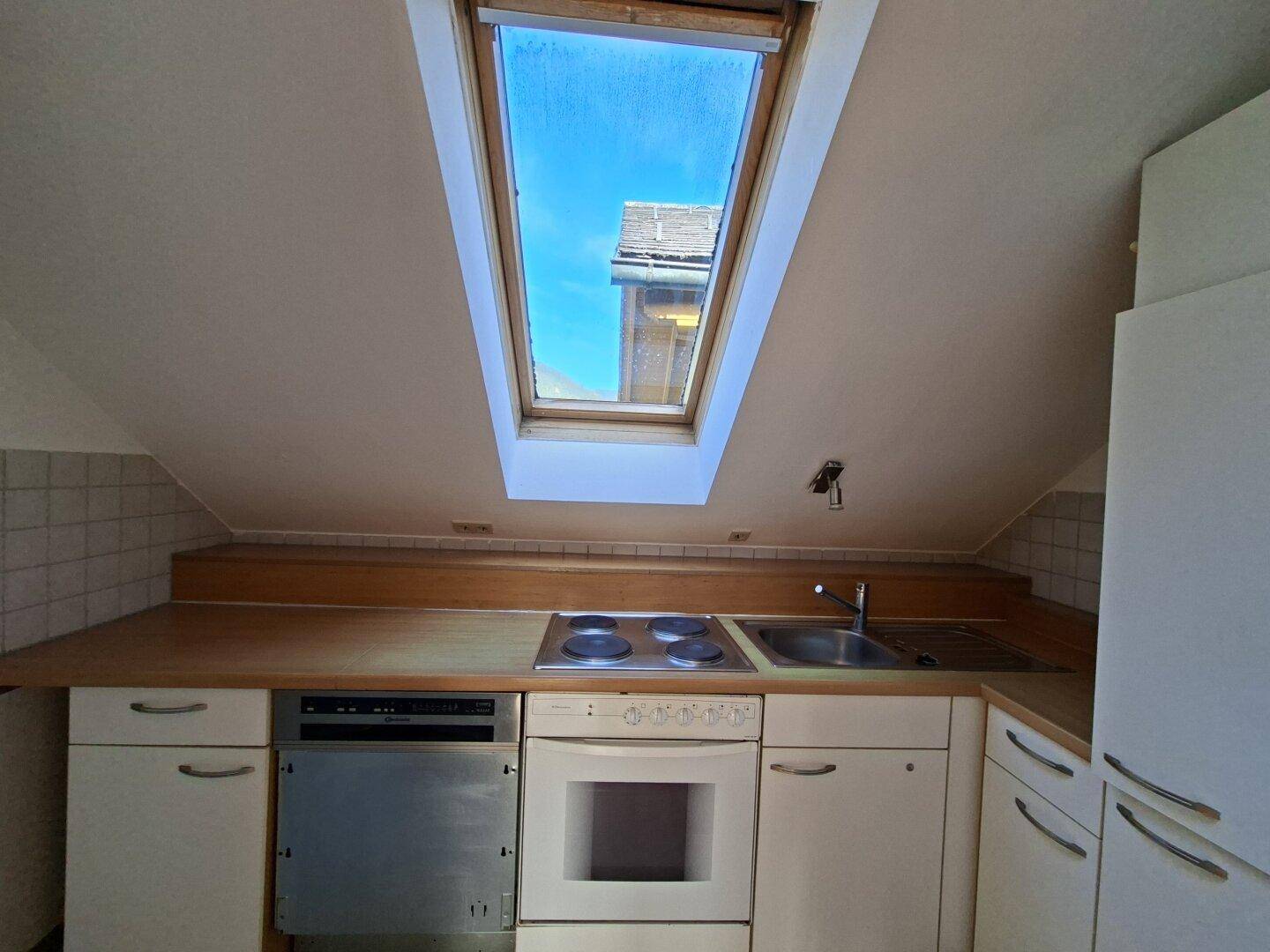 Dachgeschossküche mit Einbaugeräten, Holz-Arbeitsplatte und einem großen Dachfenster für viel Tageslicht.