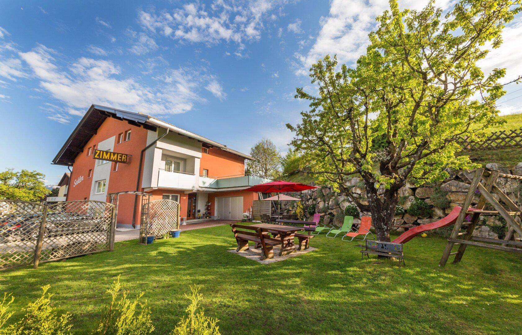 Ein großer Gartenbereich mit Spielplatz, Holzbänken und einem Sonnenschirm, ideal für Familien.