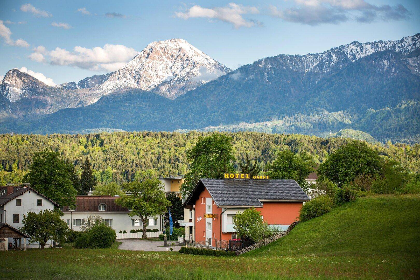 Das Hotelgebäude liegt idyllisch vor einer beeindruckenden Bergkette mit schneebedeckten Gipfeln.