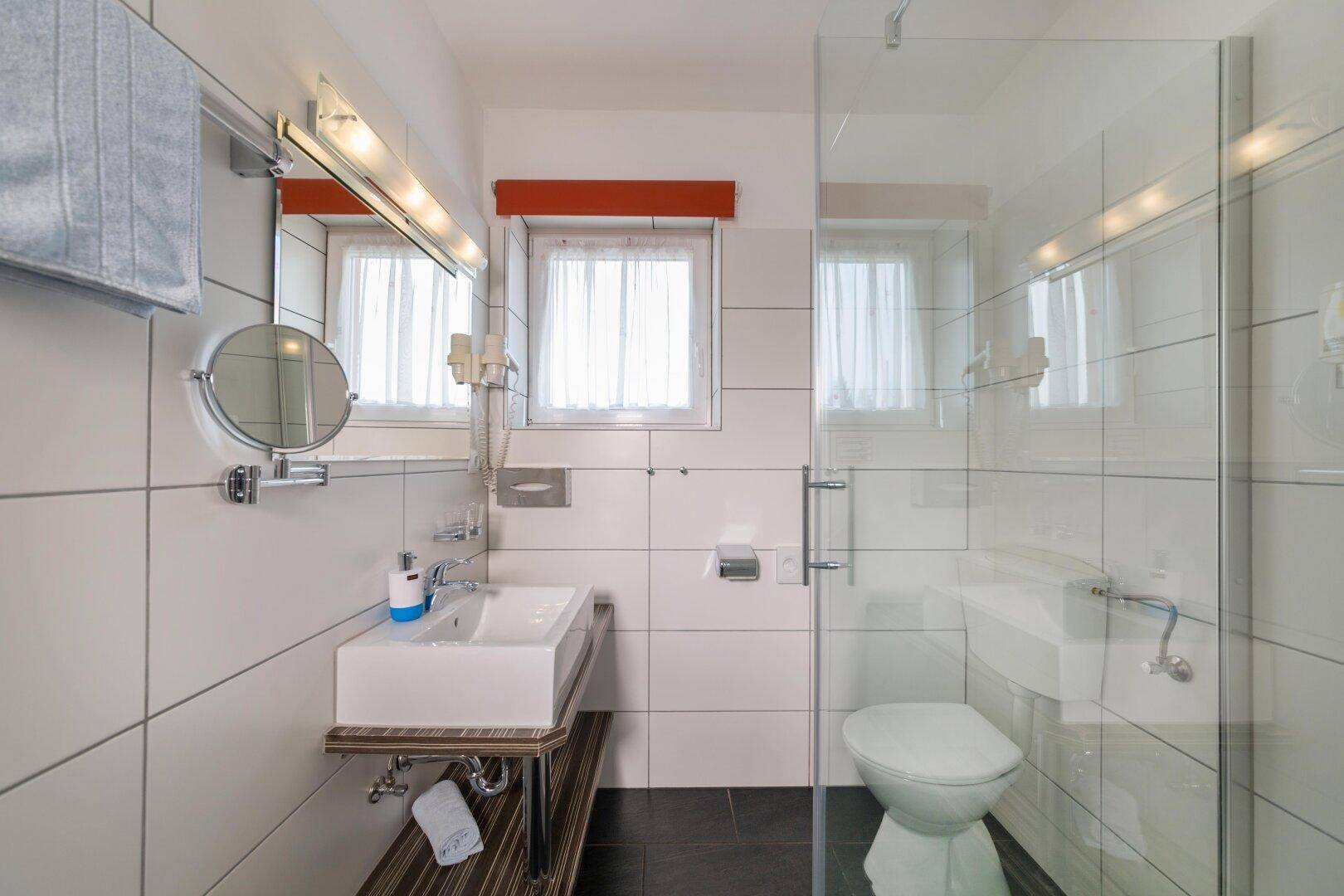 Modernes Badezimmer mit Duschkabine, WC und Waschbecken auf einer Holzablage mit Fenster.