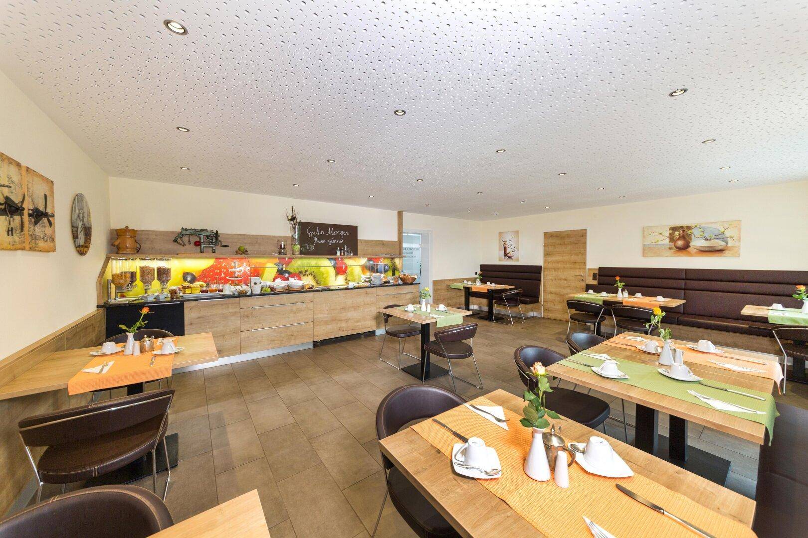 Geräumiger Frühstücksraum mit mehreren Tischen, bequemen Sitzbänken und einem Buffetbereich.