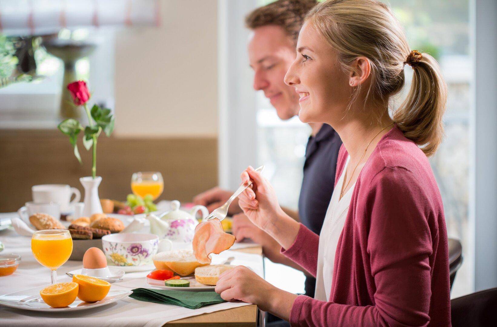 Gäste genießen ein reichhaltiges Frühstück mit frischen Säften, Eiern und Gebäck an einem gedeckten Tisch.