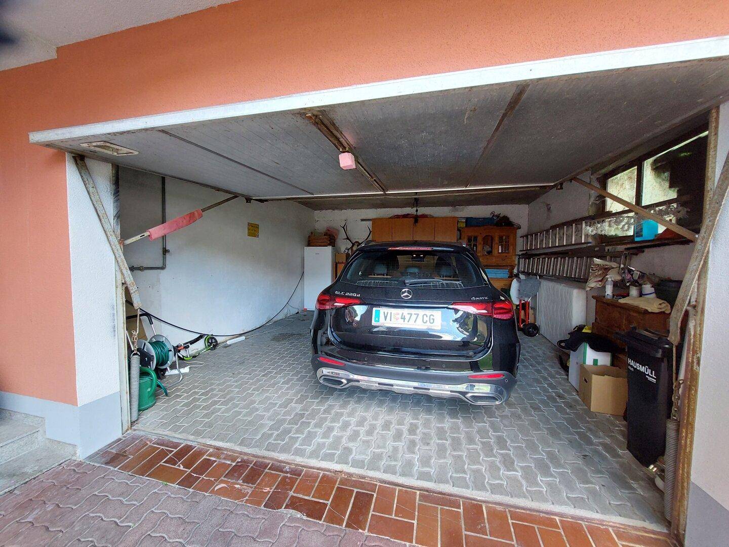 Geräumige Garage mit einem geparkten Auto, Fliesenboden und Stauraum.