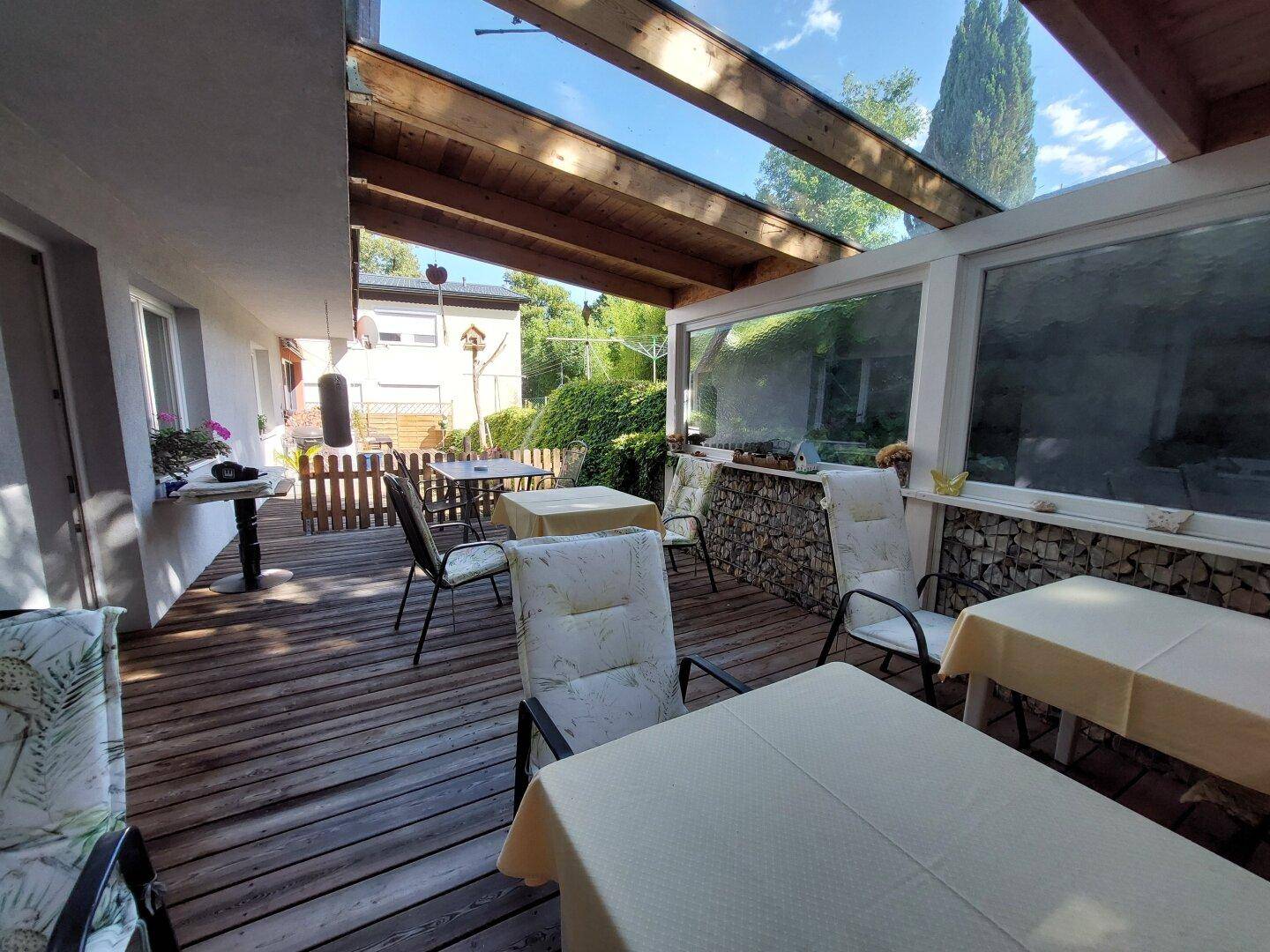 Überdachte Holzterrasse mit Tischen und Stühlen, ideal für Mahlzeiten im Freien.