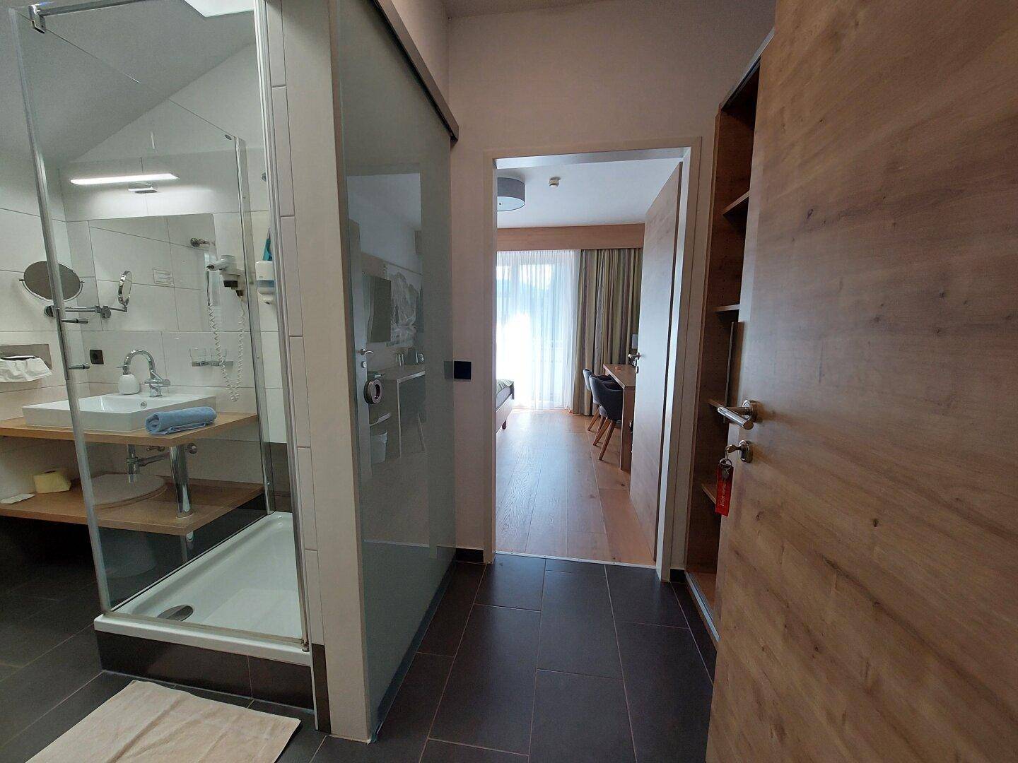 Badezimmer mit Dusche und Blick auf den Flur, der zu einem hellen Schlafzimmer führt.