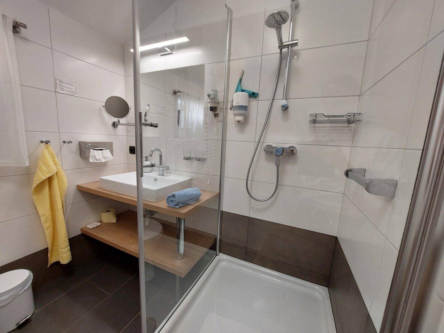 Modernes Badezimmer mit begehbarer Dusche, Waschbecken auf Holzplatte und weißen Fliesen.