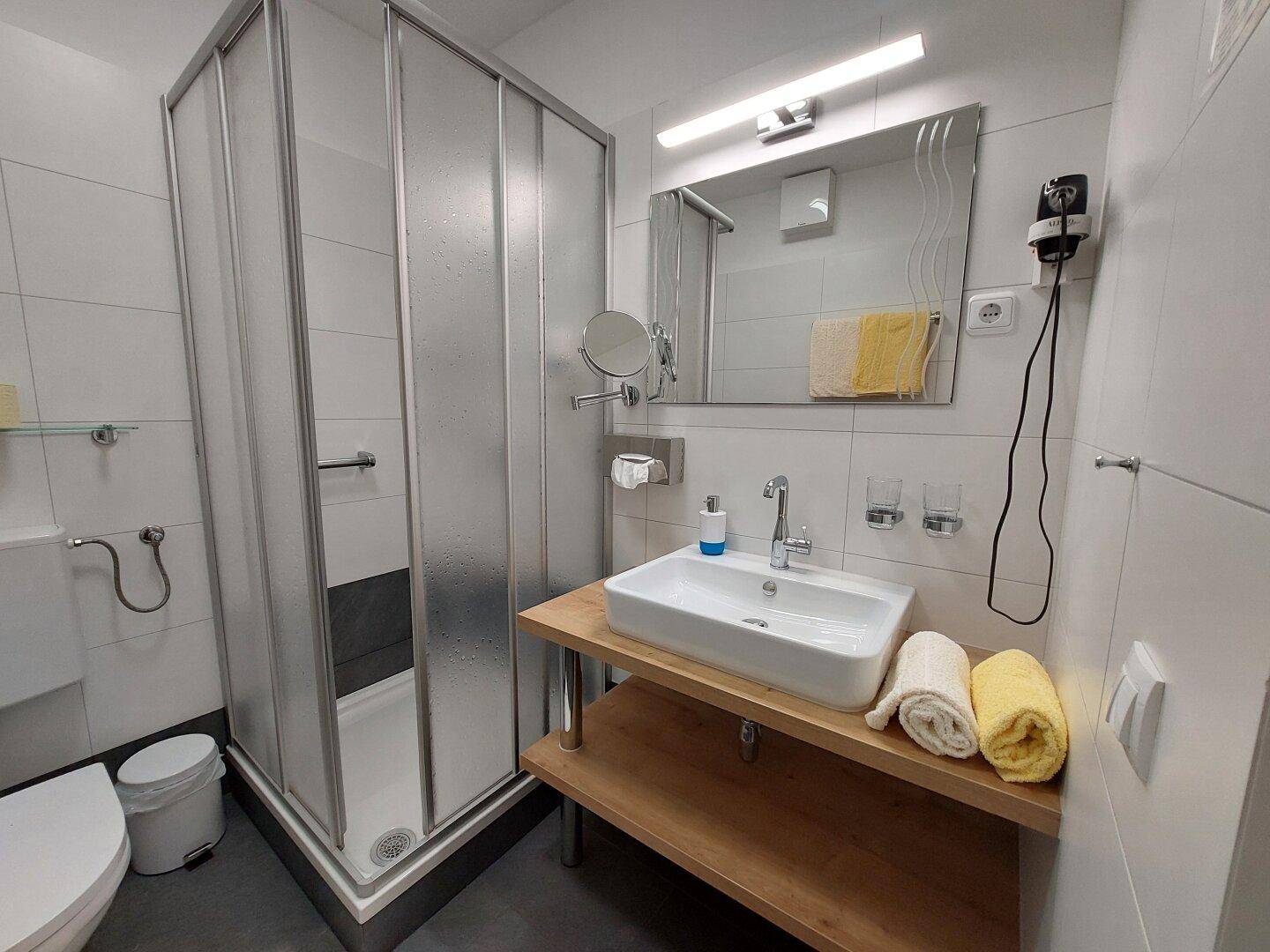 Modernes Badezimmer mit Duschkabine, Waschbecken auf Holzplatte und weißen Wandfliesen.
