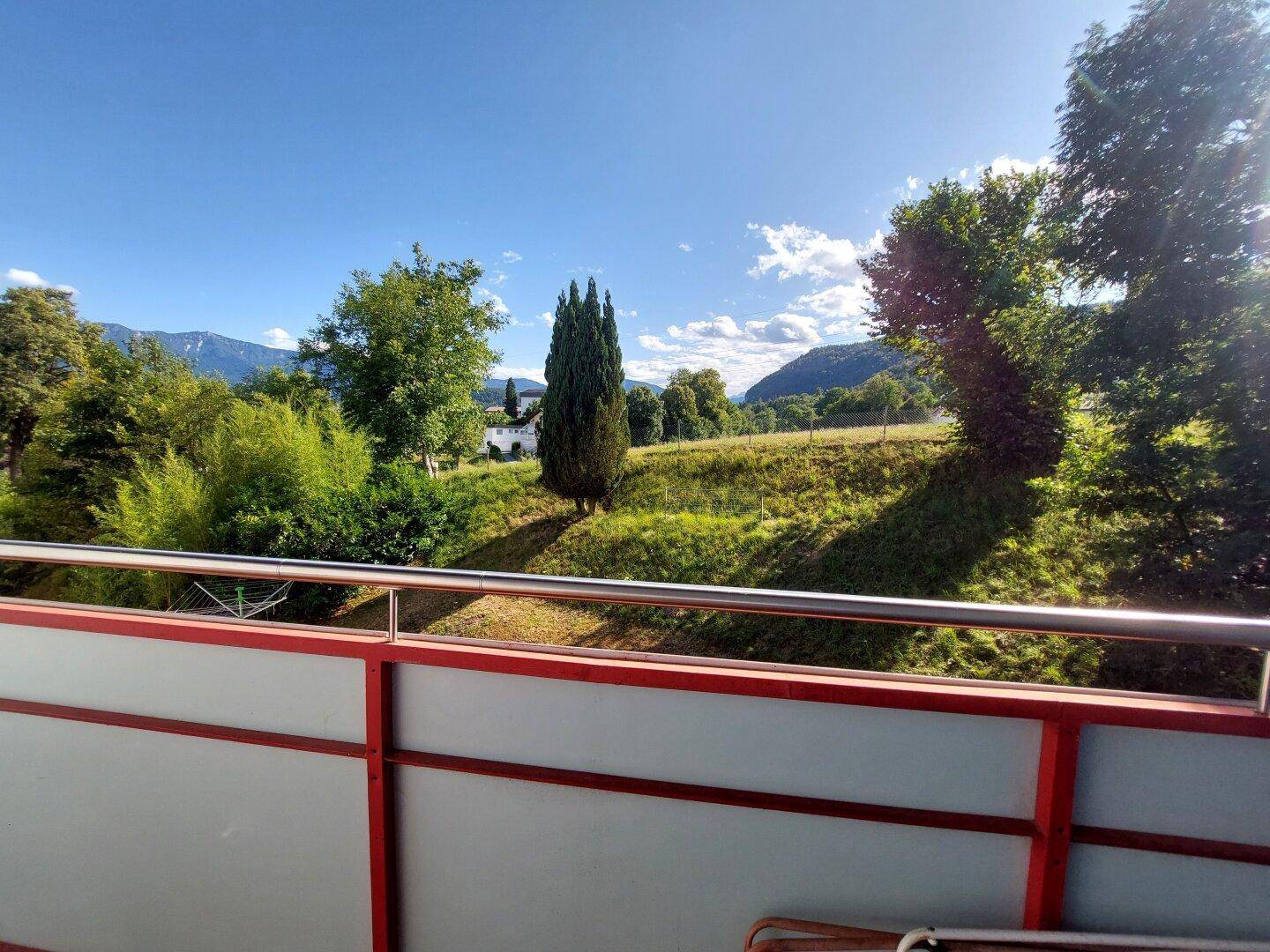 Balkon mit weitem Blick auf grüne Hügel und Bäume unter einem strahlend blauen Himmel.