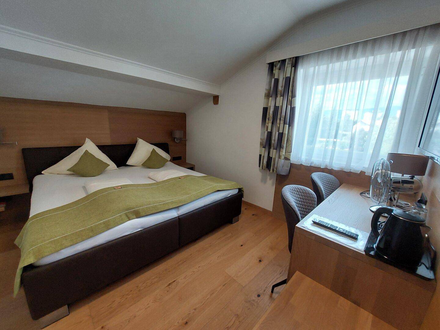 Gemütliches Schlafzimmer im Dachgeschoss mit Doppelbett, Holzboden und Schreibtisch unter der Dachschräge.