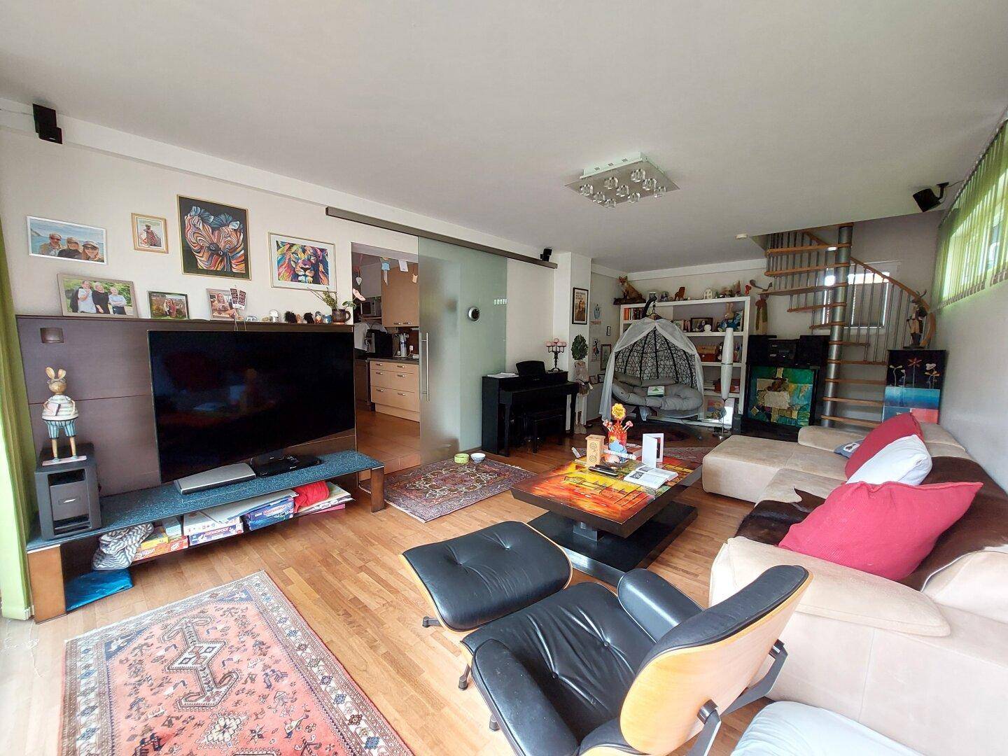 Geräumiges Wohnzimmer mit Holzboden, großem Fernseher, bequemen Sofas und Wendeltreppe.