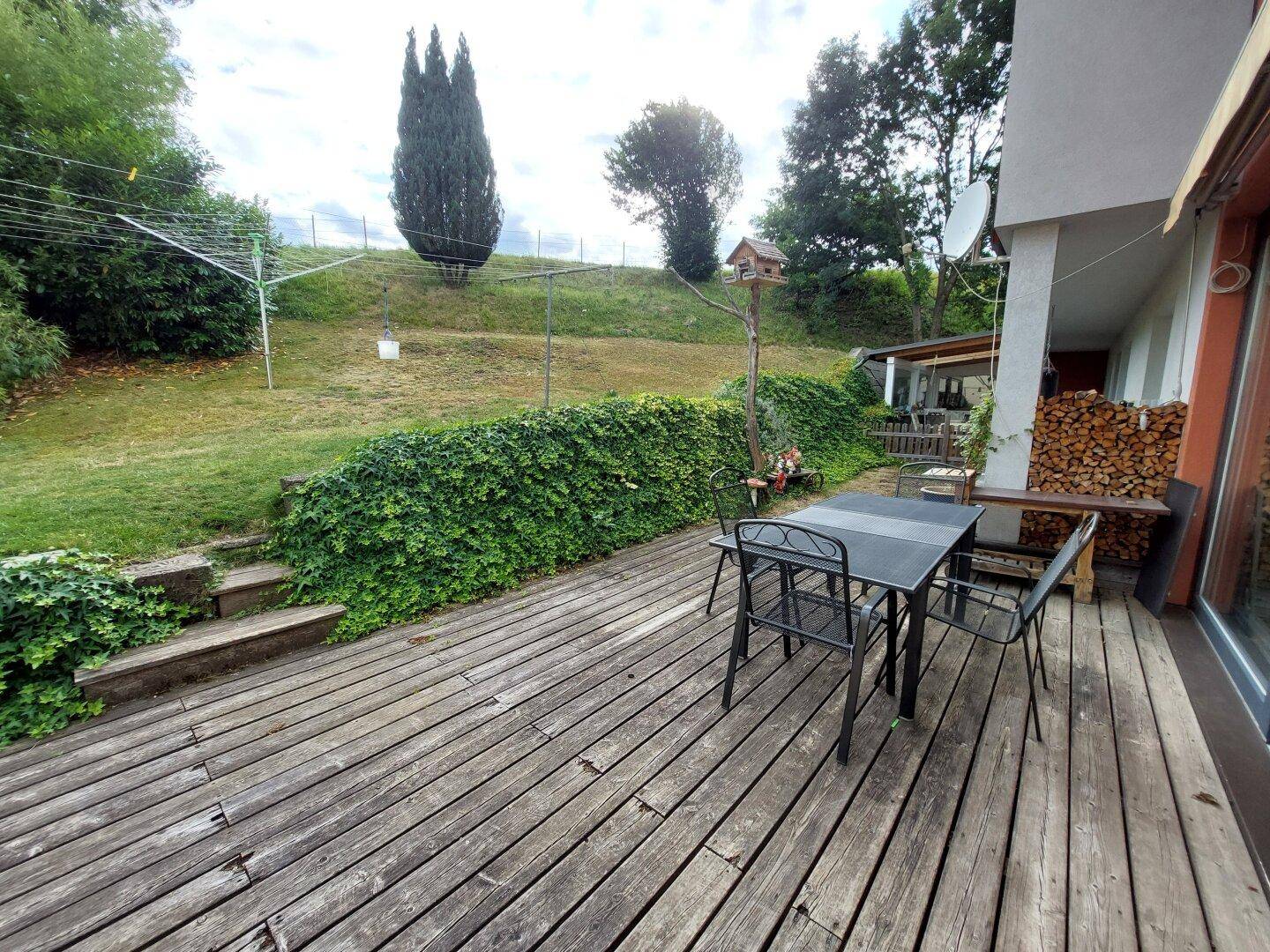 Große Holzterrasse mit Gartenmöbeln und Blick auf den grünen Gartenbereich.