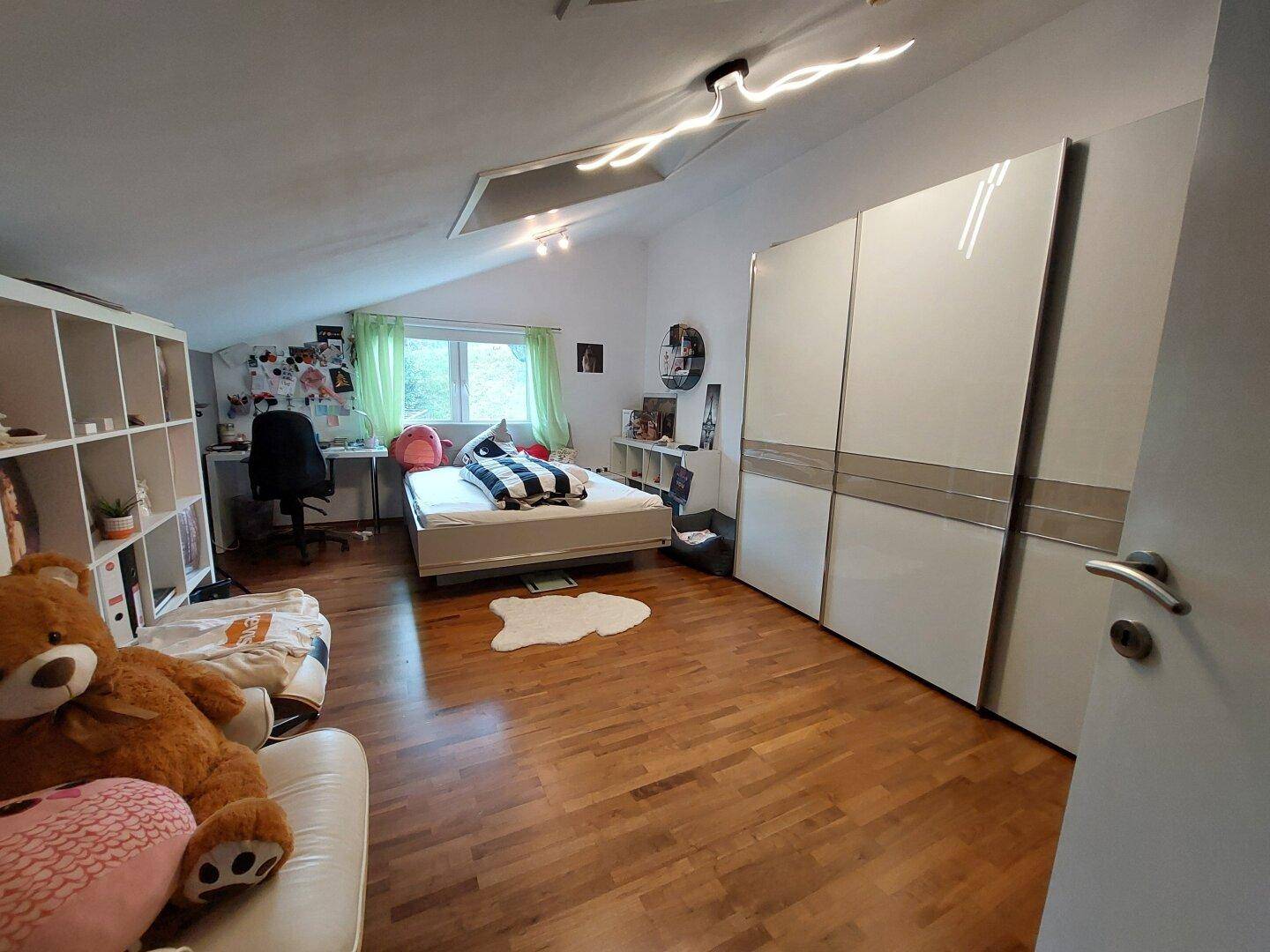 Geräumiges Schlafzimmer im Dachgeschoss mit Holzboden, großem Kleiderschrank und Schreibtisch.