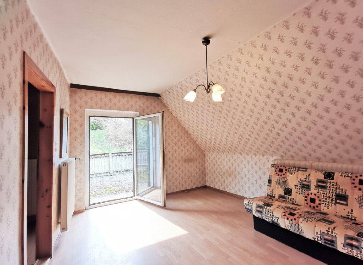 Helles Zimmer mit Dachschräge, gemusterter Tapete und direktem Zugang zu einem Balkon.