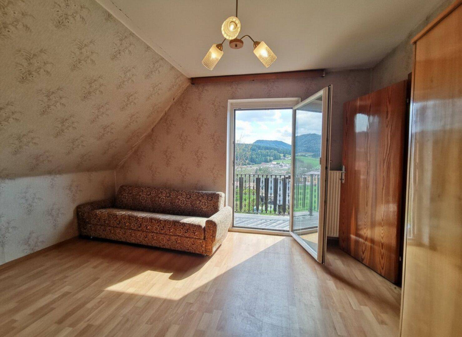 Helles Zimmer mit Dachschräge, Sofa und direktem Zugang zu einem Balkon mit schöner Aussicht.