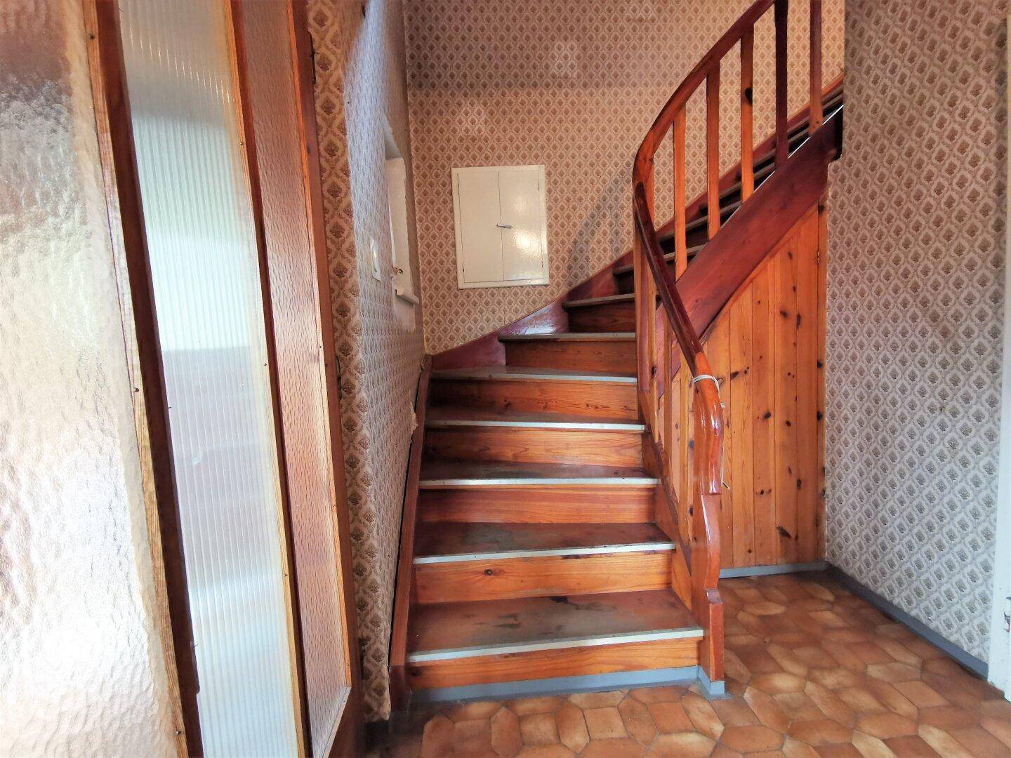 Treppenhaus mit Holztreppe und gemusterter Tapete, das die Stockwerke in rustikalem Stil verbindet.