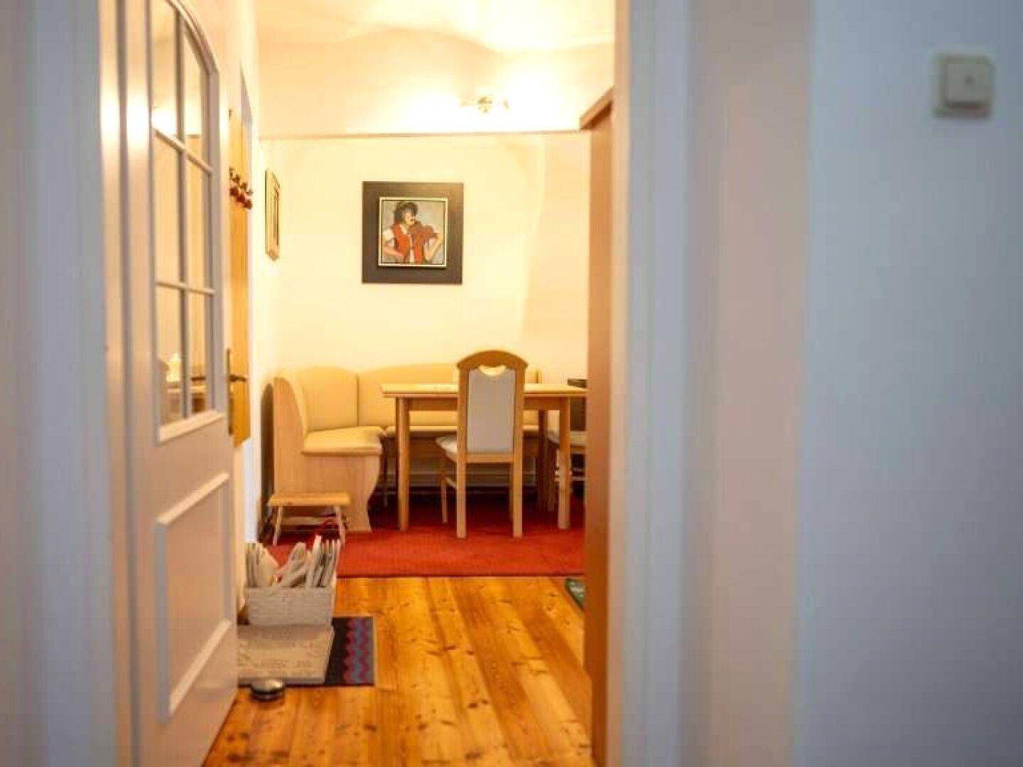 Gemütlicher Essbereich mit Holztisch, Sitzbank und Parkettboden, sichtbar durch eine offene Tür.