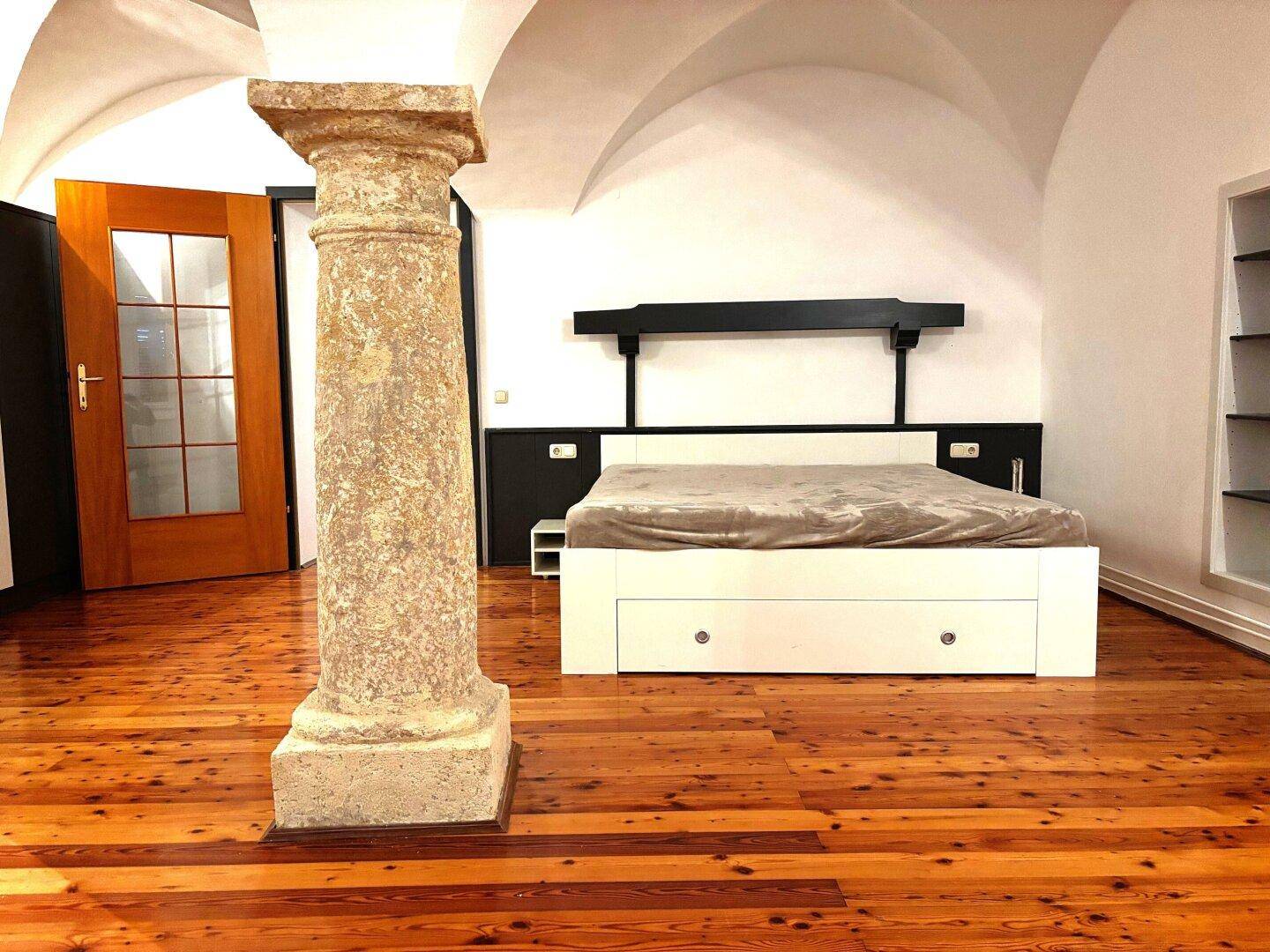 Geräumiges Schlafzimmer mit beeindruckender Gewölbedecke, Holzboden und einer antiken Steinsäule.