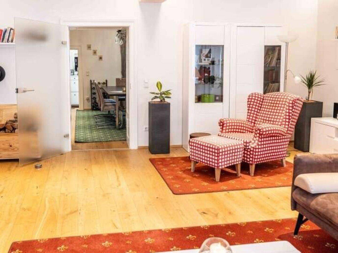 Helles Wohnzimmer mit Holzfußboden, rotem Teppich und einem bequemen, karierten Sessel.