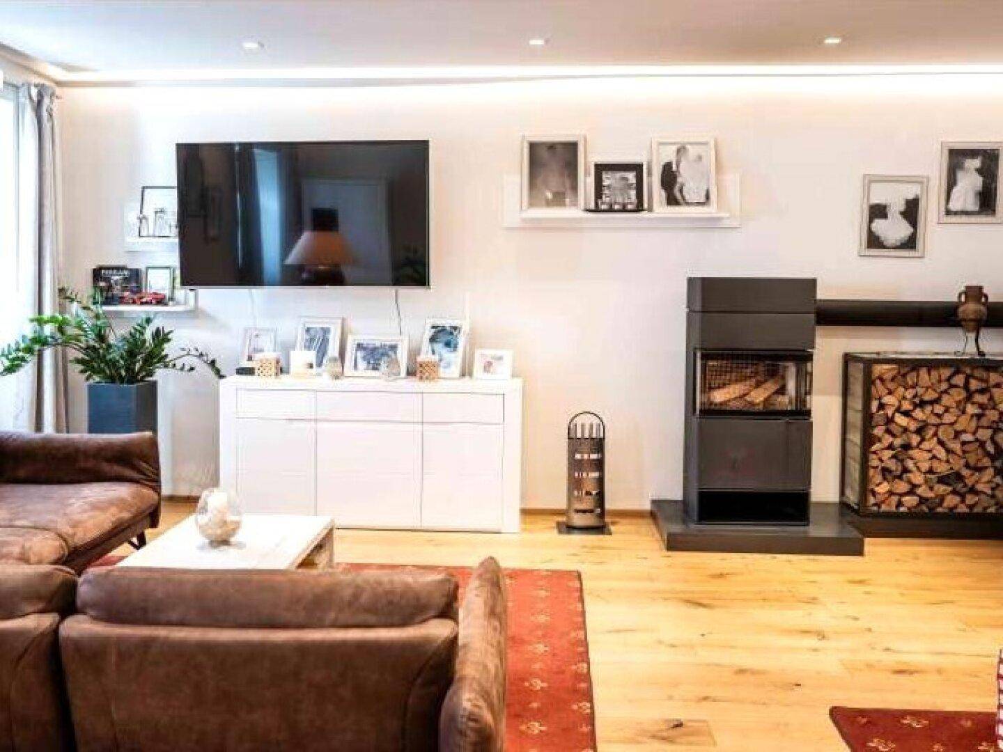 Modernes Wohnzimmer mit Kamin, großem Fernseher und bequemen Sofas auf hellem Holzfußboden.