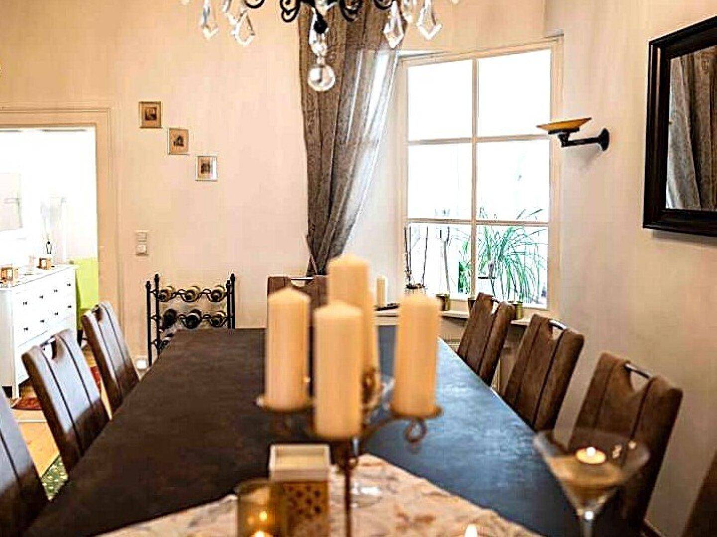 Eleganter Essbereich mit großem Holztisch, Kronleuchter und einem Fenster mit Blick nach draußen.