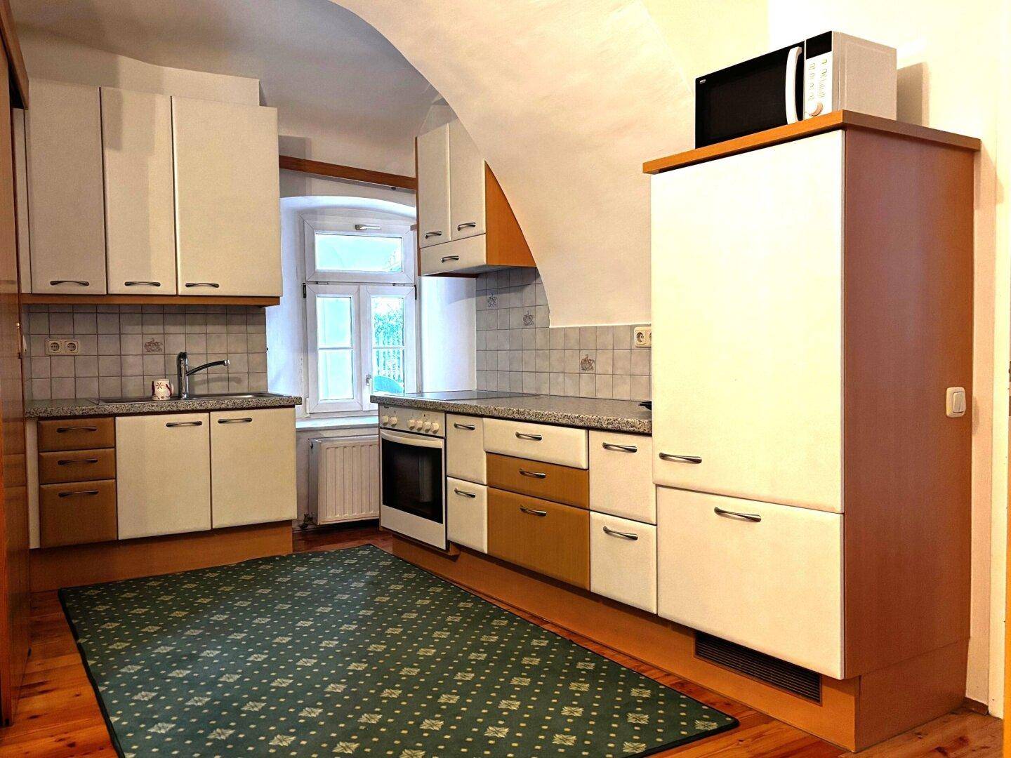 Traditionelle Küche mit Holzschränken, Fliesenrückwand und einem Fenster mit Blick ins Grüne.