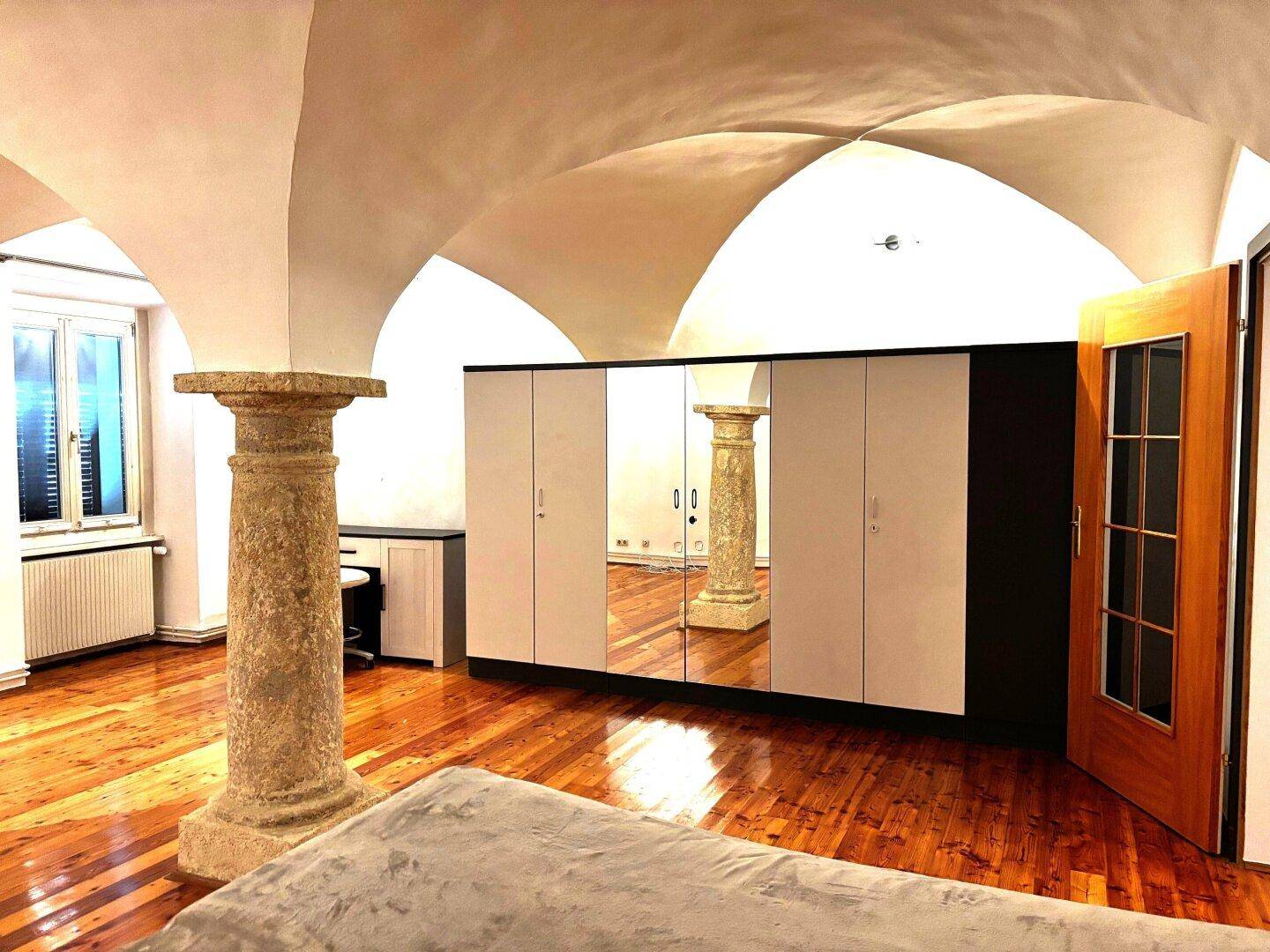 Großes Schlafzimmer mit Gewölbedecke, Holzboden und einem modernen Spiegelschrank.
