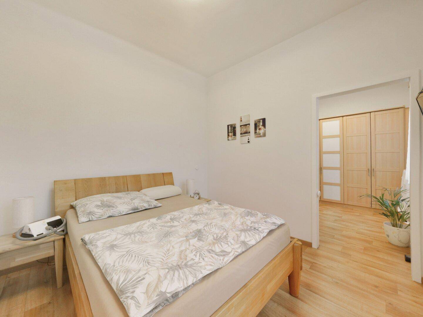Helles Schlafzimmer mit Holzbett, Laminatboden und Zugang zu einem weiteren Raum.