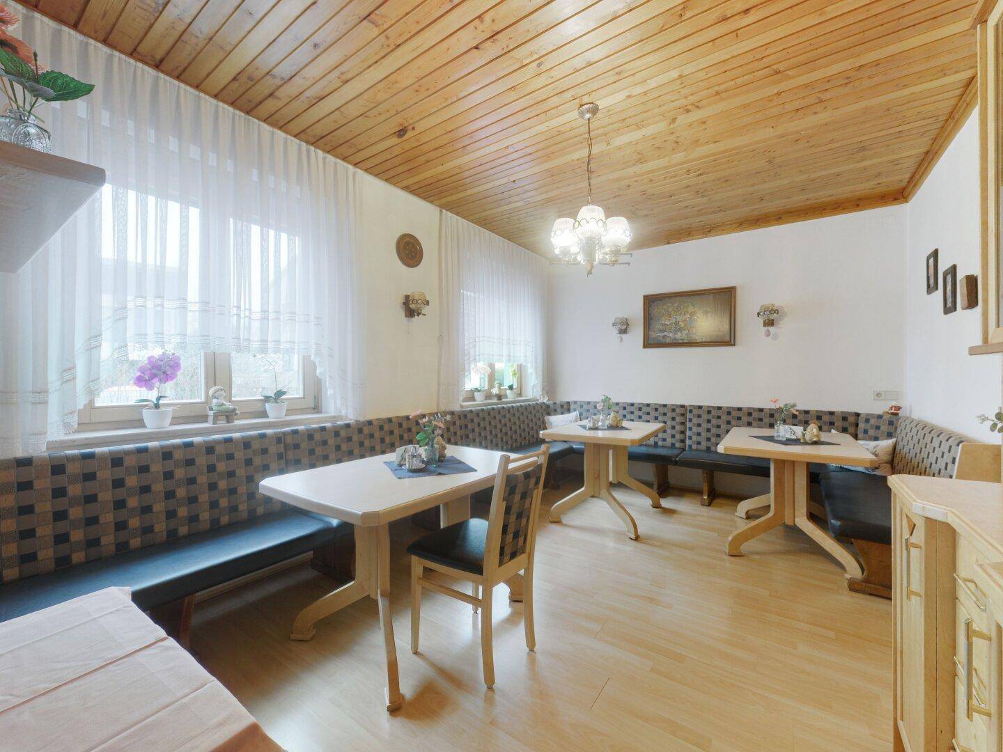 Gemütlicher Essbereich mit Holztäfelung an der Decke, gepolsterten Bänken und mehreren Tischen.