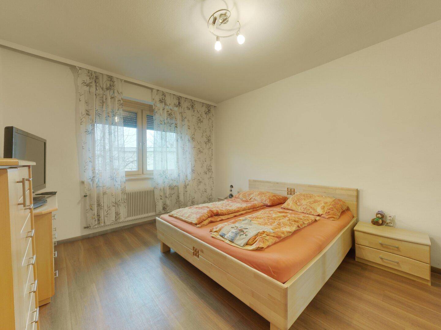 Gemütliches Schlafzimmer mit Holzboden, Doppelbett und einem Fenster mit Vorhängen.