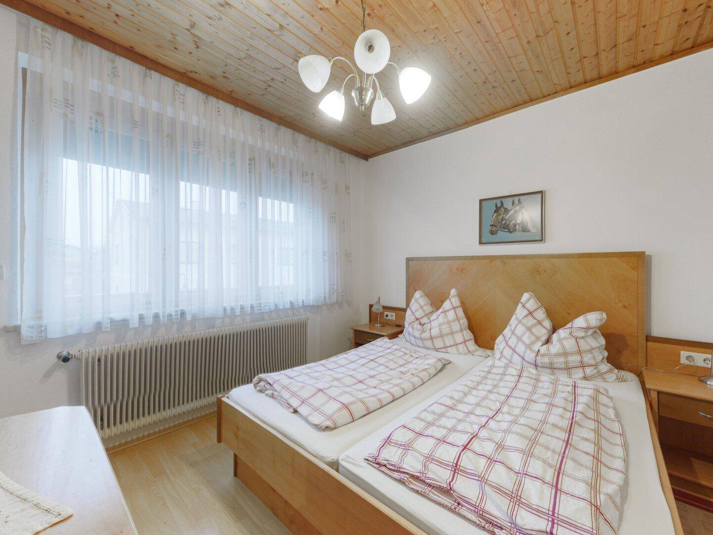 Helles Schlafzimmer mit Holzboden, Doppelbett und einer Holzdecke im traditionellen Stil.