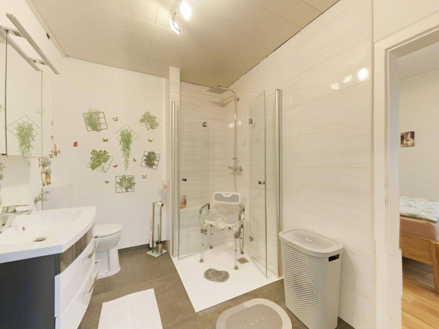 Modernes Badezimmer mit ebenerdiger Dusche, weißen Fliesen und einem Waschbecken mit Spiegelschrank.