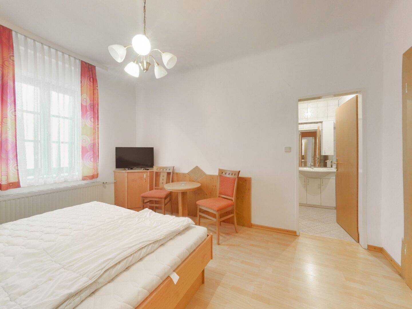 Schlafzimmer mit Doppelbett, Holzboden und direktem Zugang zu einem angrenzenden Badezimmer.