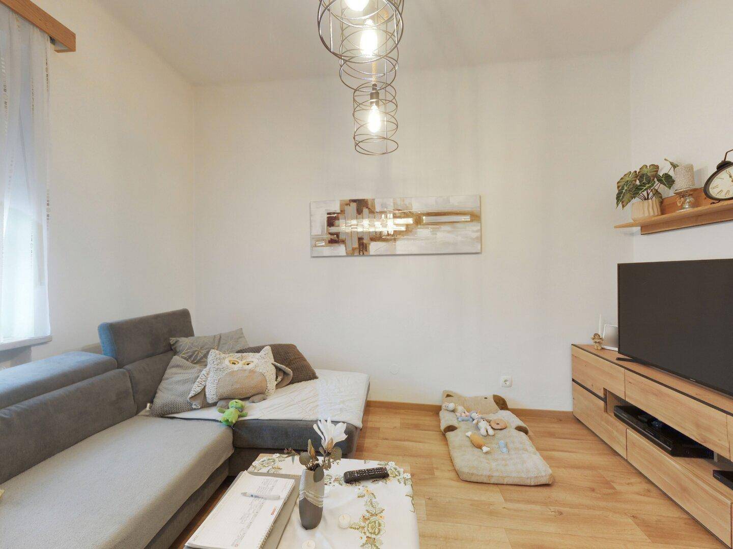 Modernes Wohnzimmer mit Ecksofa, Holzboden und zeitgenössischer Wanddekoration.
