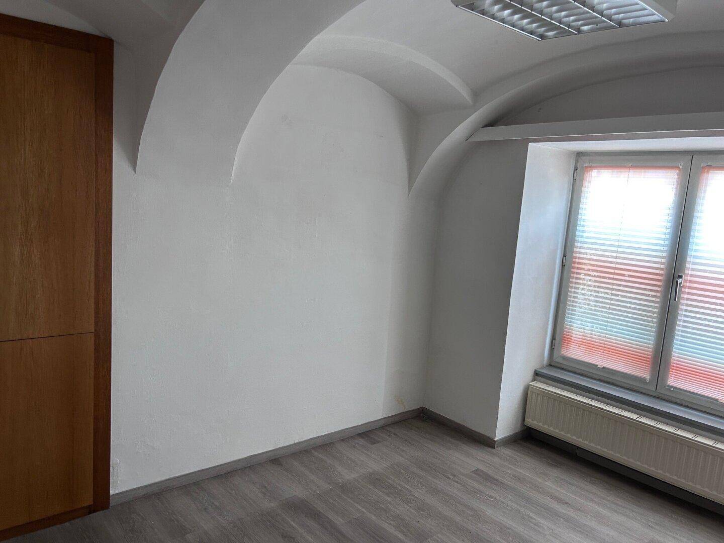 Büroraum mit Gewölbedecke, Laminatboden und einem großen Holzschrank.