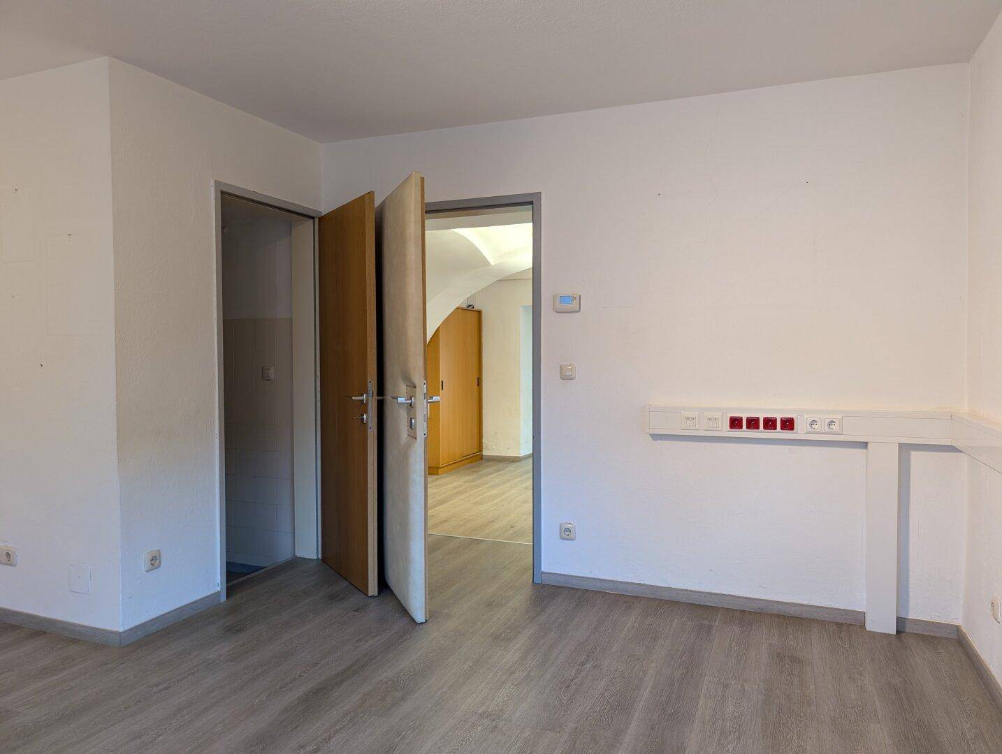Heller Büroraum mit Laminatboden und Türen zu angrenzenden Räumen.