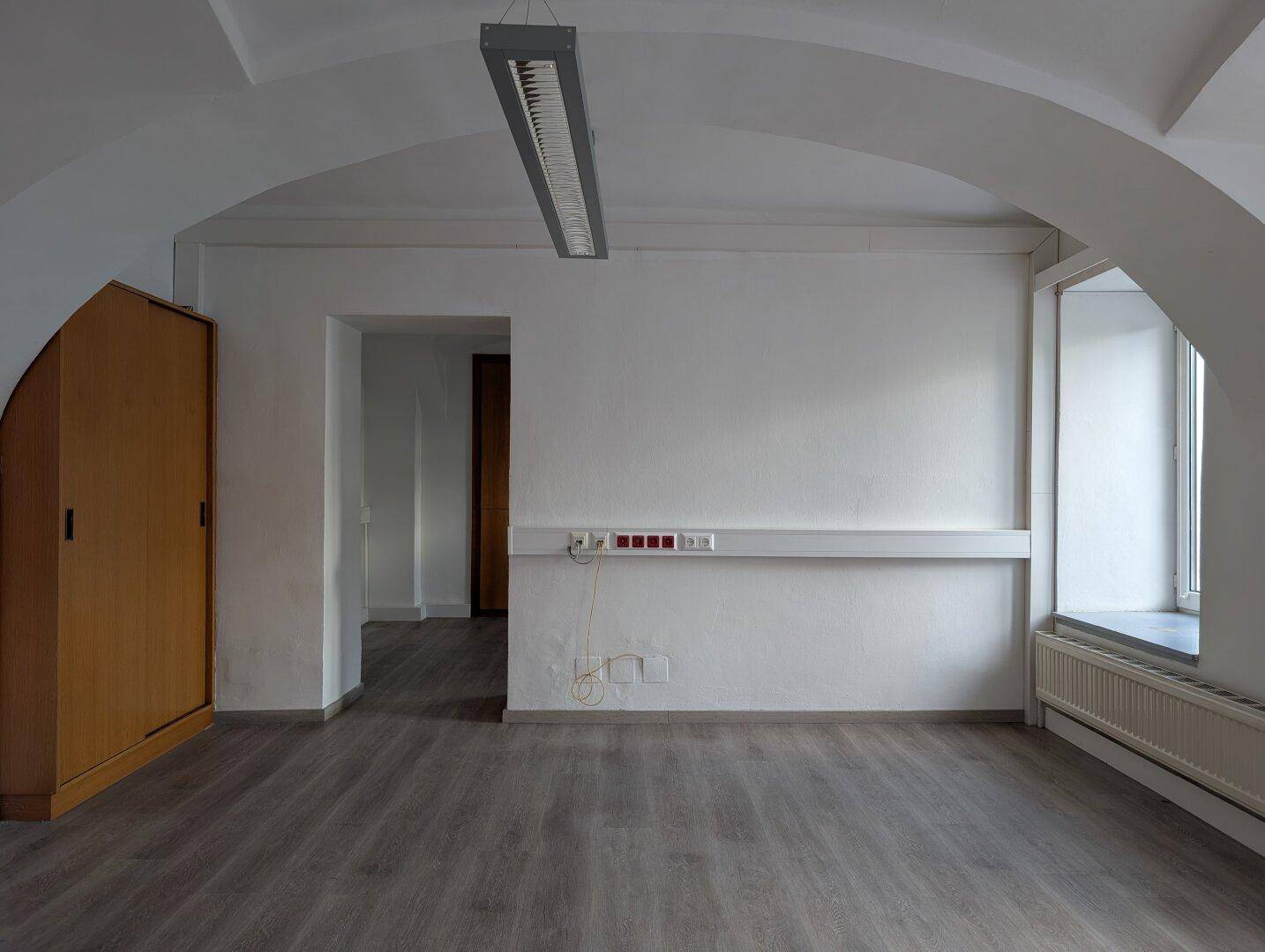 Büroraum mit Gewölbedecke, Laminatboden und einem großen Holzschrank.