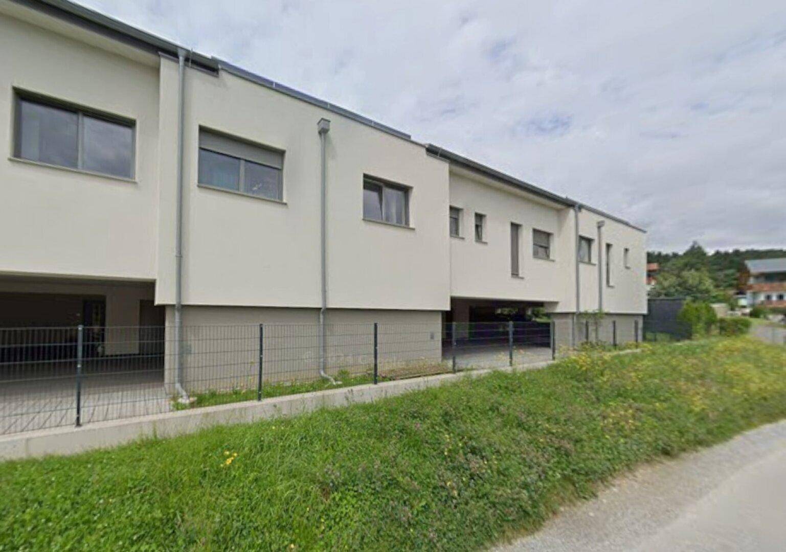 Moderne Reihenhäuser mit weißer Fassade und Fenstern, umgeben von Grünflächen.