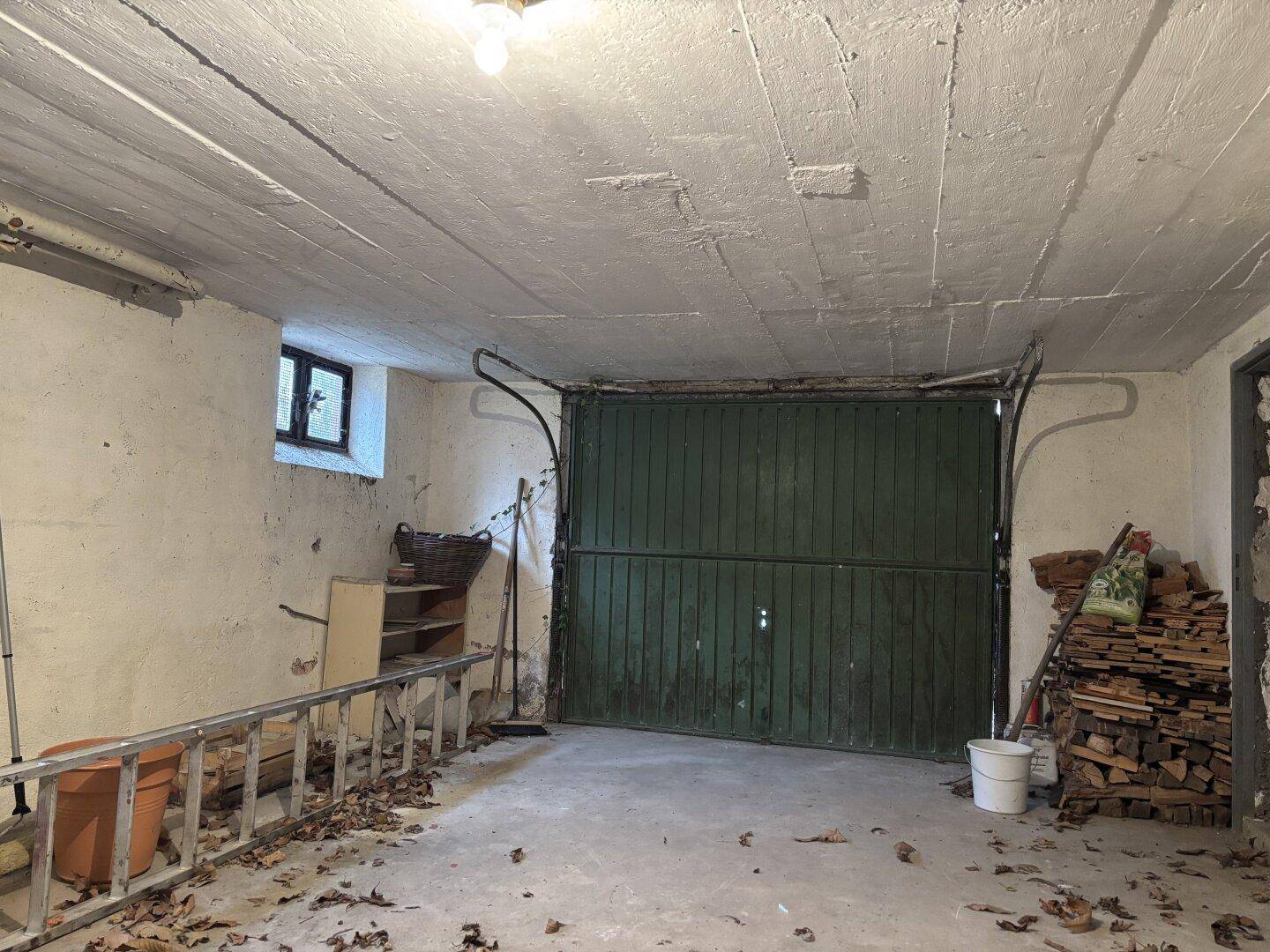 Geräumige Garage im Kellergeschoss mit großem Tor und Betonboden.