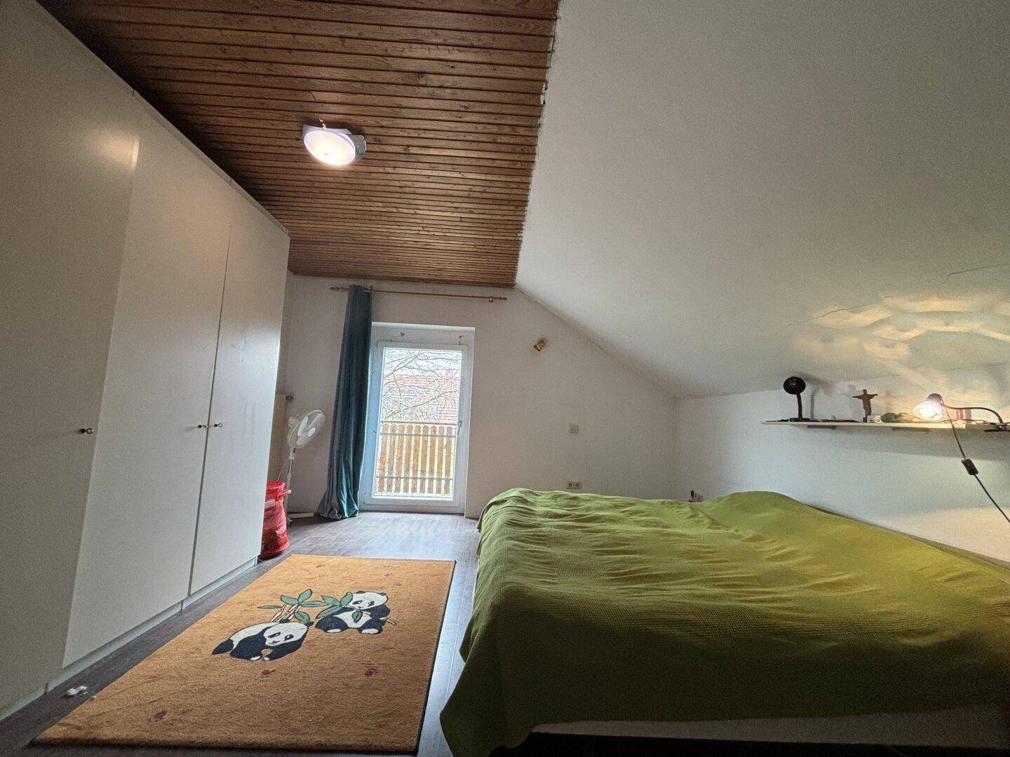 Schlafzimmer im Dachgeschoss mit Holzbalkendecke, Einbauschränken und Balkonzugang.