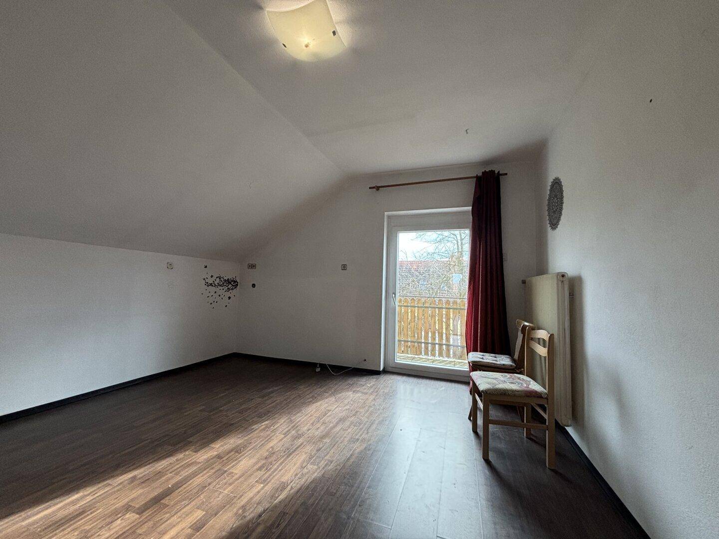 Heller Wohnbereich im Dachgeschoss mit Laminatboden und Zugang zu einem Balkon.
